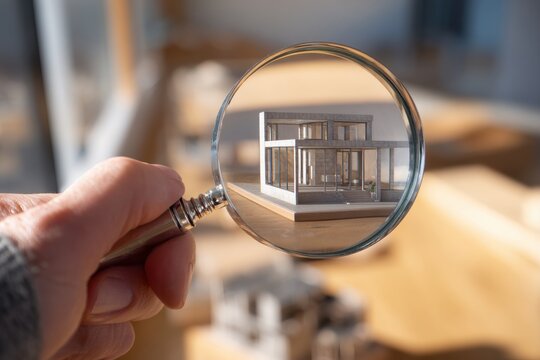 Hand holding magnifying glass over modern house model daylight