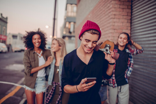 Young friends with skateboard walking on urban street at sunset