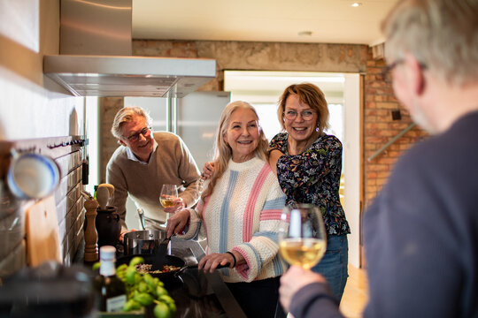 Happy senior friends cooking and drinking wine in cozy home kitchen