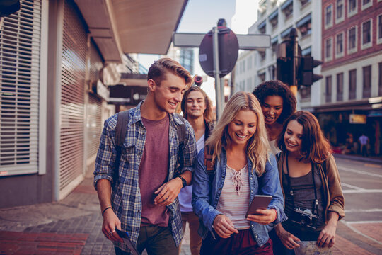 Group of friends using smartphone while walking on city street