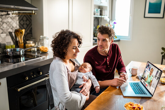 Young parents video calling doctor in home kitchen with newborn baby