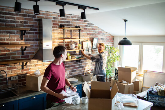 Two men unpacking boxes and decorating kitchen at home