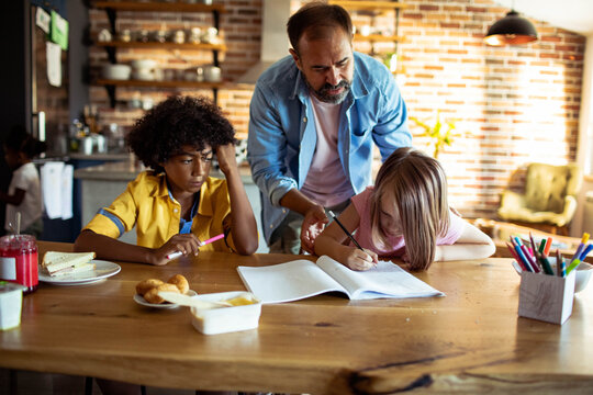 Father helping kids with homework at kitchen table