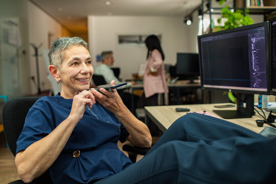 Smiling mature woman using voice assistant at office desk