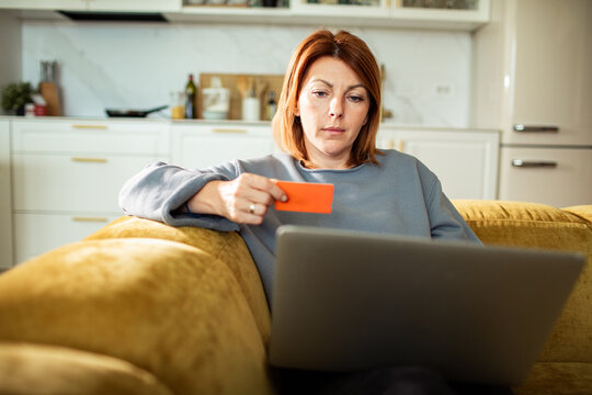 Woman holding credit card and using laptop on couch at home