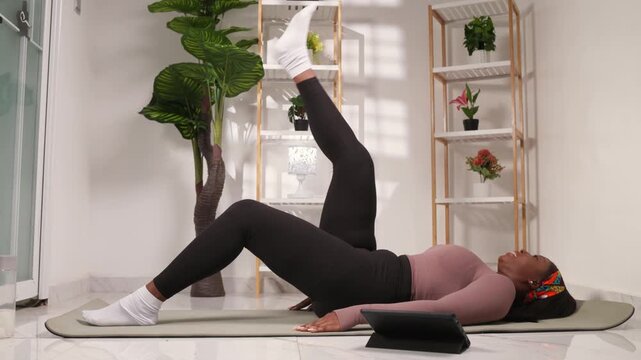 African woman doing leg lift on yoga mat following online workout
