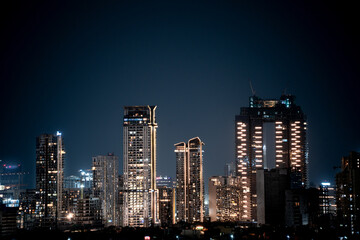 Naklejka premium Modern highrise multi storey skyscrapers at night with lights shining through showcasing growth of apartments, buildings, houses and shopping centers in cities like gurgaon, delhi, bangalore, hyderaba