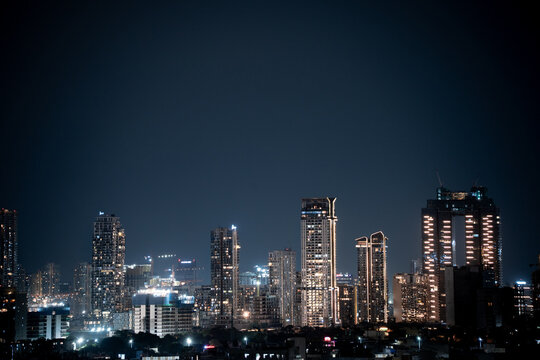 Modern highrise multi storey skyscrapers at night with lights shining through showcasing growth of apartments, buildings, houses and shopping centers in cities like gurgaon, delhi, bangalore, hyderaba