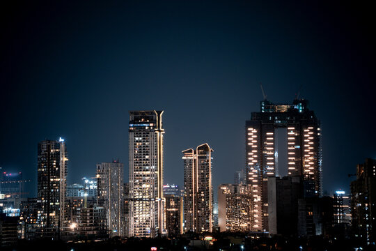 Modern highrise multi storey skyscrapers at night with lights shining through showcasing growth of apartments, buildings, houses and shopping centers in cities like gurgaon, delhi, bangalore, hyderaba