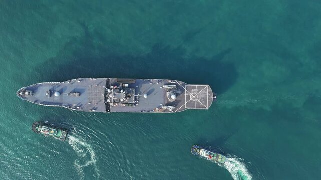 large naval amphibious assault ship being assisted by tugboats in the strategic Strait of Hormuz. Concept of maritime security, naval power projection, and protection of international shipping lanes.