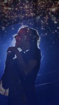 Vertical video: Singer hair-flipping, moving to mic on music stage, singing amid blue light stars