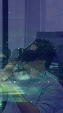 Vertical video: Man adjusting VR headset at desk, gesturing to control glowing UI for tech demo