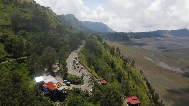 4K aerial view of Bromo volcanic valley, winding roads, and tourists at a scenic mountain viewpoint.