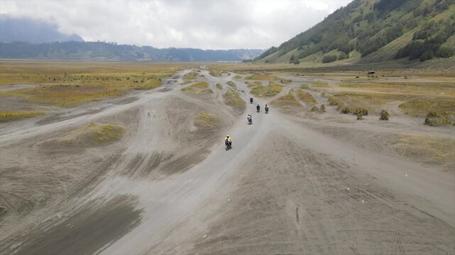 4K aerial view of motorbikes crossing the vast Bromo volcanic sand sea with mountain backdrop.