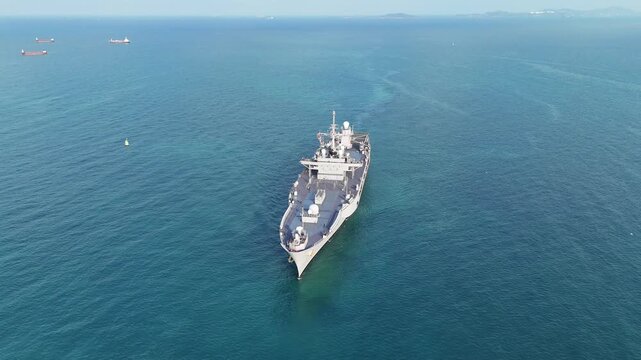 large naval amphibious assault ship being assisted by tugboats in the strategic Strait of Hormuz. Concept of maritime security, naval power projection, and protection of international shipping lanes.