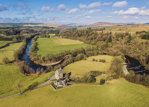 The River Esk winds through green fields and dense trees near Gilnockie Tower in the Scottish Borders. This scene shows a clear view of the landscape near Langholm on the A7