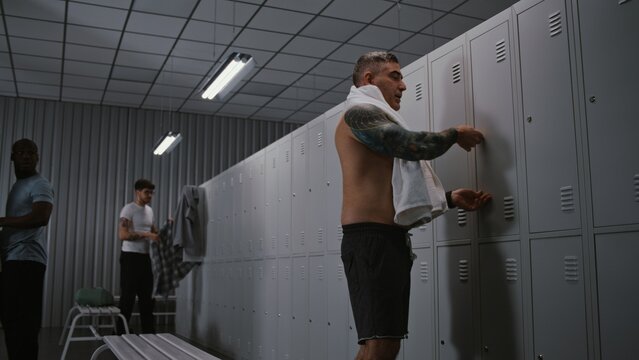Mature, Athletic Male Officer With Arm Tattoos Undresses, Takes White Towel From Locker, and Heads to Shower After Finishing Airport Security Duty. Concept of Shift End in Staff Locker Room.