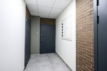 Fototapeta premium modern hallway with grey metal doors, brick accent wall, white paneled ceiling, light grey tiled floor, intercom panel, minimalist design, clean lines, neutral tones