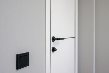 Fototapeta premium sleek white interior door with a modern black handle and lock, adjacent to a black wall switchplate, set against a light grey wall