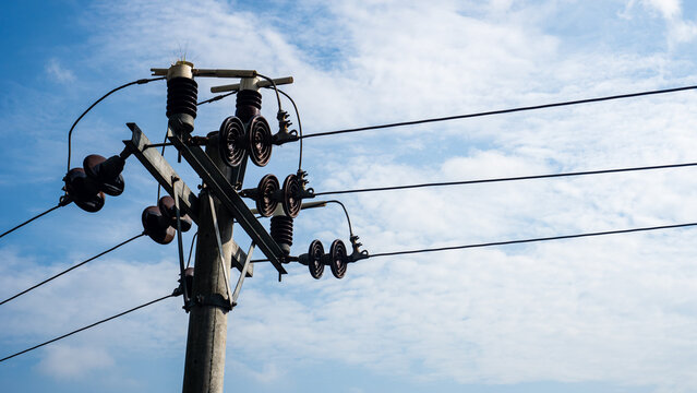 Electricity distribution pole with cables and ceramic insulators under cloudy sky. Industrial utility background.
