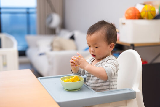 Baby sitting on high chair eating corn at home