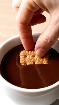 Hand dipping a biscuit into a cup of hot chocolate