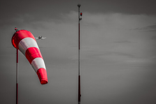 Red and white windsock at an airfield with a small airplane in the background