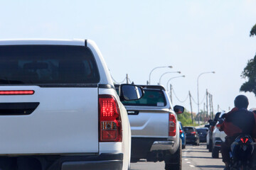 Rear view of vehicles congested on a highway during the day, highlighting taillights and a motorcycle rider © Lukman Riyadi