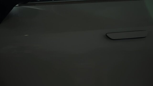 Close-up side view of a modern grey car showcasing flush door handles, smooth body contours, metallic paint reflections, and a sporty rear wheel design under studio lighting