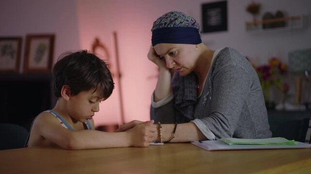 Mother guiding son through homework at table in evening, attentive parenting and home learning routine, support and concentration in quiet family study moment