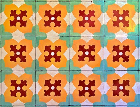 Vintage ceramic floor tiles featuring a geometric floral pattern. The weathered surface shows vibrant orange, red, and green tones, capturing a classic Mediterranean or colonial aesthetic