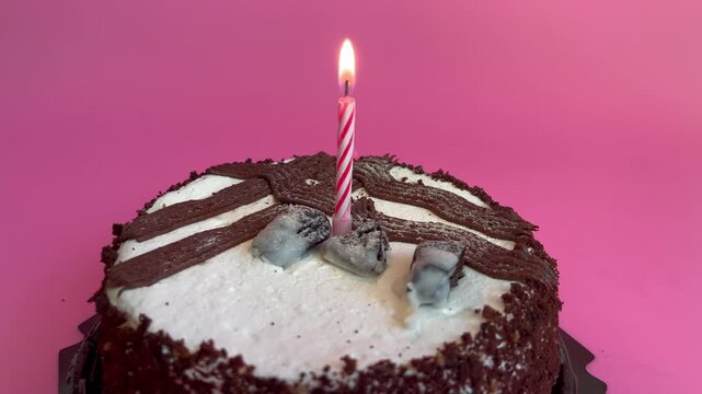 Chocolate birthday cake with a lit candle on top, featuring decorative frosting and a pink background, showcasing the cake, 1 year, one year old