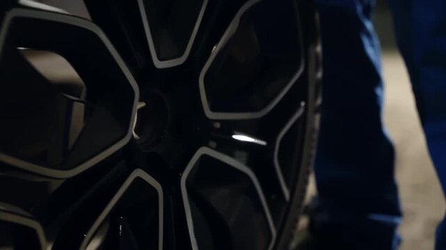 Close-up of a mechanic in blue workwear tightening lug nuts on a black alloy wheel with a torque wrench, then a low-angle view of the tire contacting the concrete garage floor