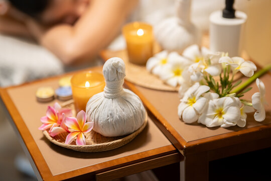 Herbal compress with candles and tropical flowers on wooden tray in spa setting.