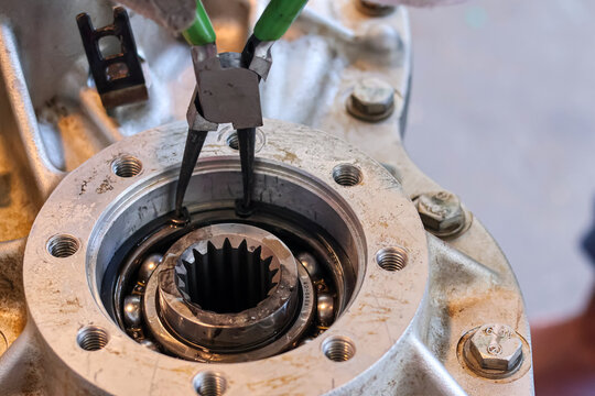 A close-up shot showing the precision use of snap ring pliers to install or remove a retaining ring inside a metal mechanical bearing assembly.