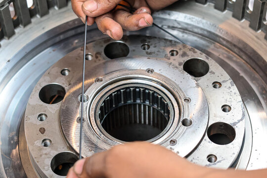 A close up shot of a technician's hands carefully fitting a thin black rubber o-ring seal onto a precision machined industrial metal component during gearbox assembly.