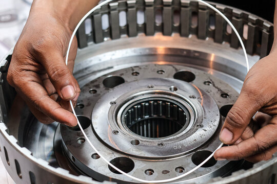 Close up shot of a technician's hands carefully fitting a large white rubber seal ring into the housing of an industrial metallic transmission gearbox during assembly.