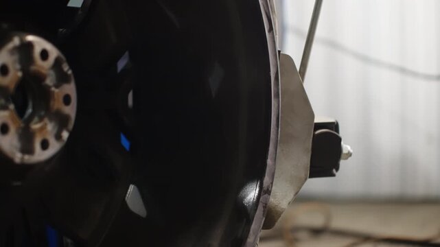 Close-up of automotive wheel hub and rim undergoing alignment measurement with a dial indicator bracket in a workshop, focusing on lug holes, metal surfaces, and precision setup