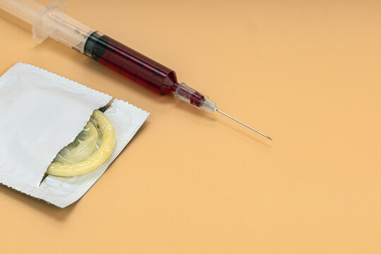 Open Condom Packet and Blood-Filled Medical Syringe Placed Together on Warm Orange Background Representing Sexual Health, HIV Transmission Risk, and STI Prevention Awareness Concept