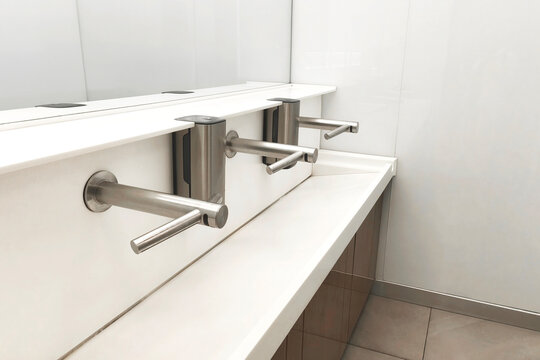 Minimalist public restroom with sleek stainless steel faucets and a white counter, emphasizing cleanliness, hygiene, and modern interior design.