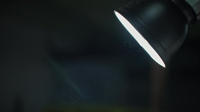 Close-up of a lone spotlight casting a bright beam into a dark room, revealing floating dust particles shimmering in the air, with motion between frames emphasizing atmosphere