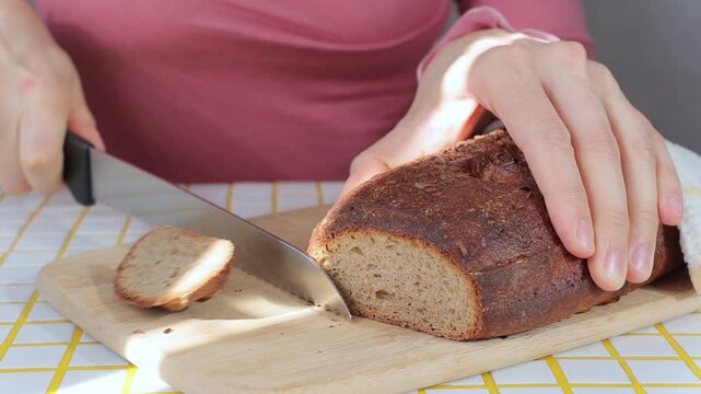 person cuts black bread on wooden board with knife. Sourdough rye bread with crispy crust. Bakery products. homemade cakes, yeast-free sourdough bread. Wholesome and healthy food. bakery.