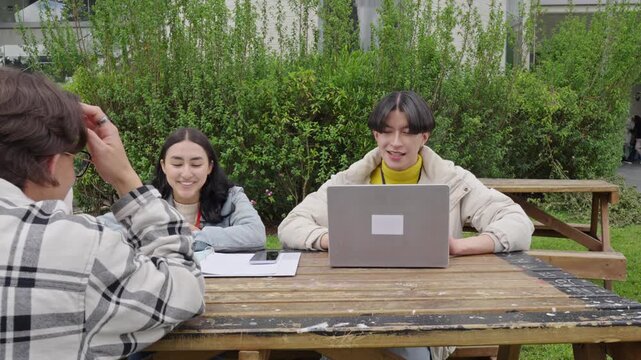 Group of young students studying together outdoors with laptop