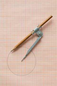 Rustic drawing compass on grid paper background vertical top view. Drafting tool for geometry education and planning design.