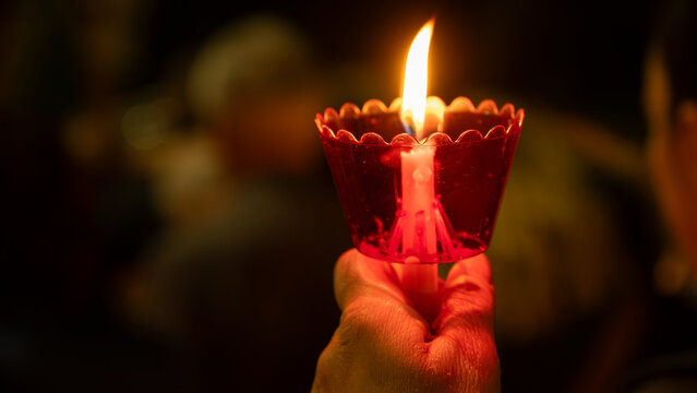 A hand holding a burning candle in a red plastic cup during a night religious vigil or ceremony, creating a warm, spiritual glow.