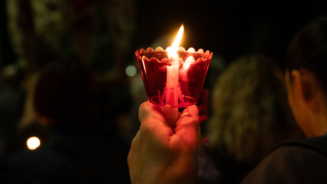 Crowd of believers holding lit candles in red cups during Orthodox Easter midnight service in Greece, celebrating the Resurrection in a spiritual night ceremony.
