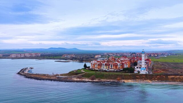 Flying over the waterscape at the coast of the Black Sea. View on the colorful Marina Cape Complex and the Aheloy lighthouse against cloudy sky.