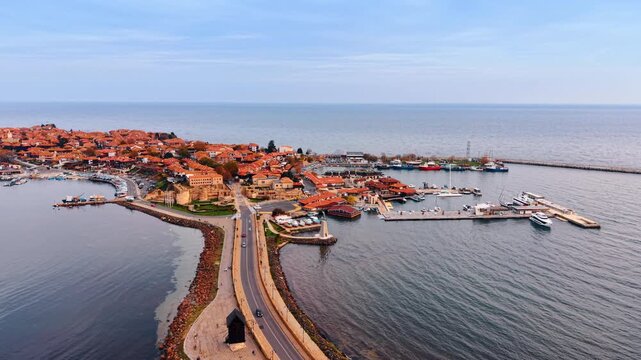 Automobiles go by the road along the isthmus. View on the peninsula with red-roofed villas in Nessebar, Bulgaria.