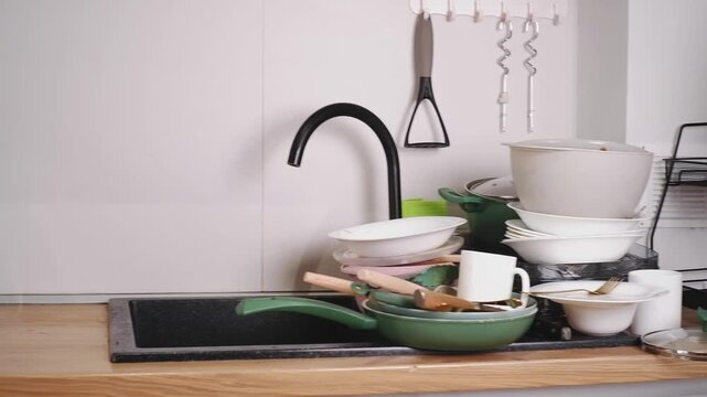 Pile of dirty dishes, plates, pans, and cutlery accumulating in a modern kitchen sink