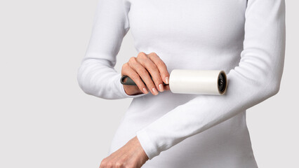Obraz premium Female cleaning white garment with adhesive roller removing visible lint from sleeve on light gray background. Concept of quick clothing refresh, polished look, fabric care routine. Copy space, banner